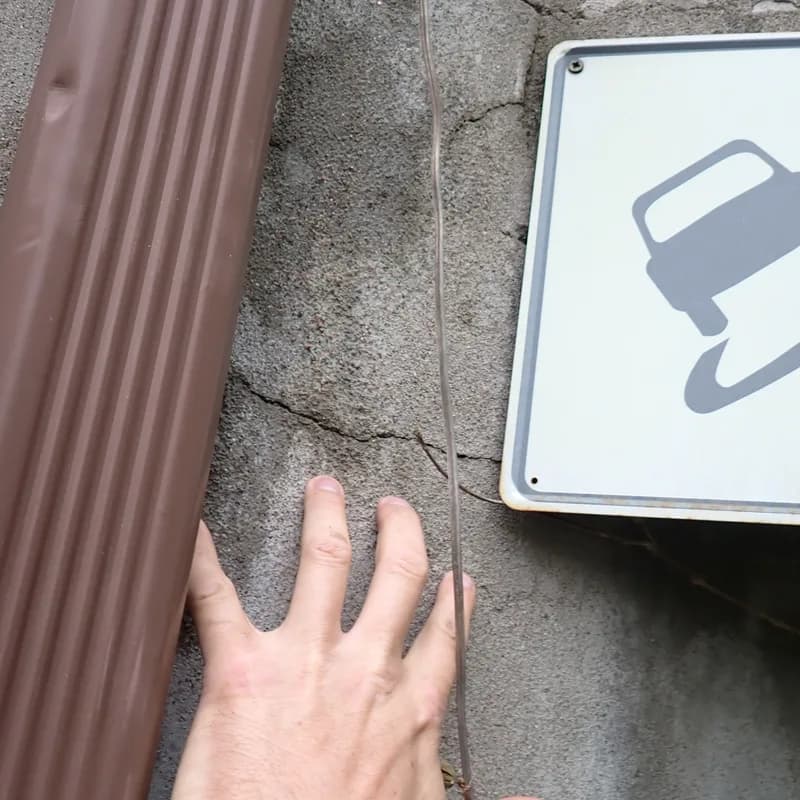 Main posée sur un mur de crépi fissuré, à côté d'une descente pluviale brune
